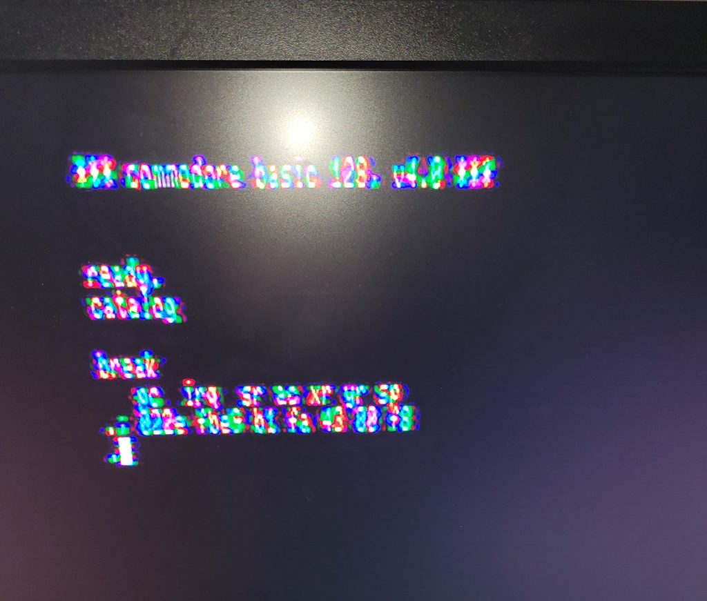A blurry artifacted photo showing the boot screen of the Commodore B128, with the "catalog" command issued, and resulting in a "break" and the resulting program code of 022e, irq fb8.