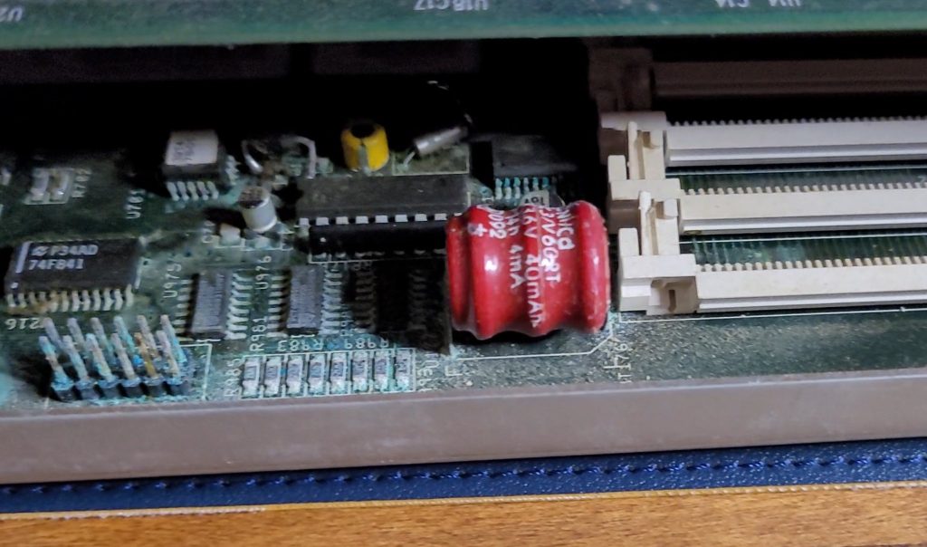 View of the clock portion of a Commodore Amiga 4000 motherboard still mounted in its case, covered in a blue-green hue due to the damage from battery leakage