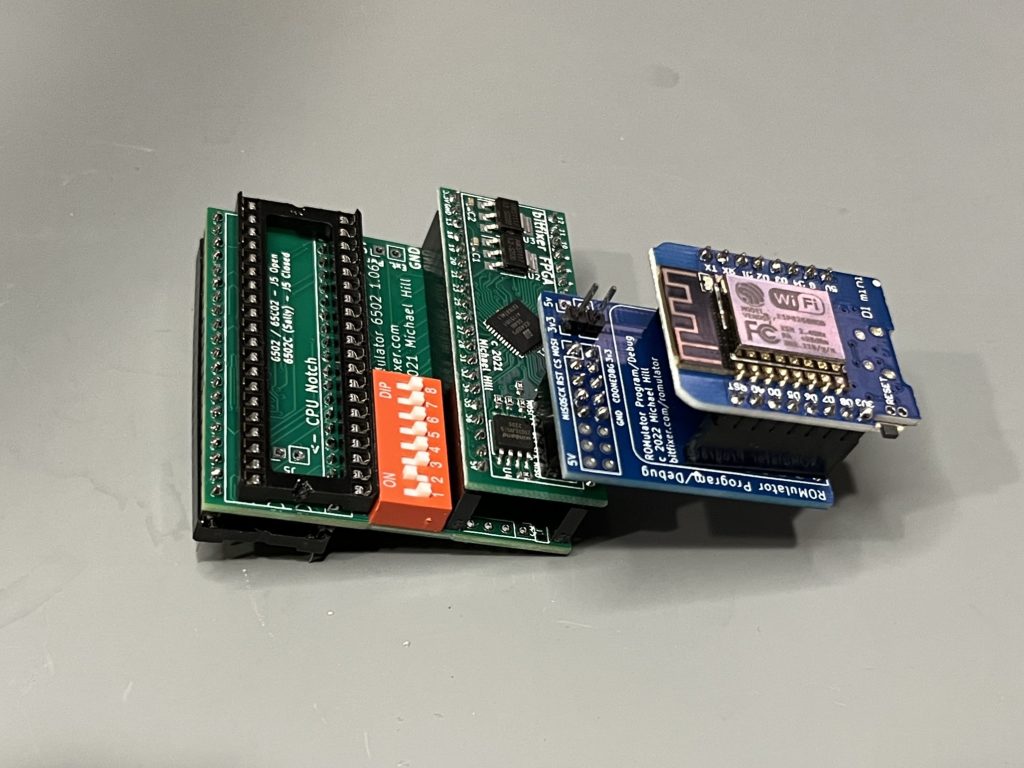 Image of an assembled ROMulator - a small green board showing a CPU socket, DIP switches, an attached FPGA board, an attached blue board containing another FPGA