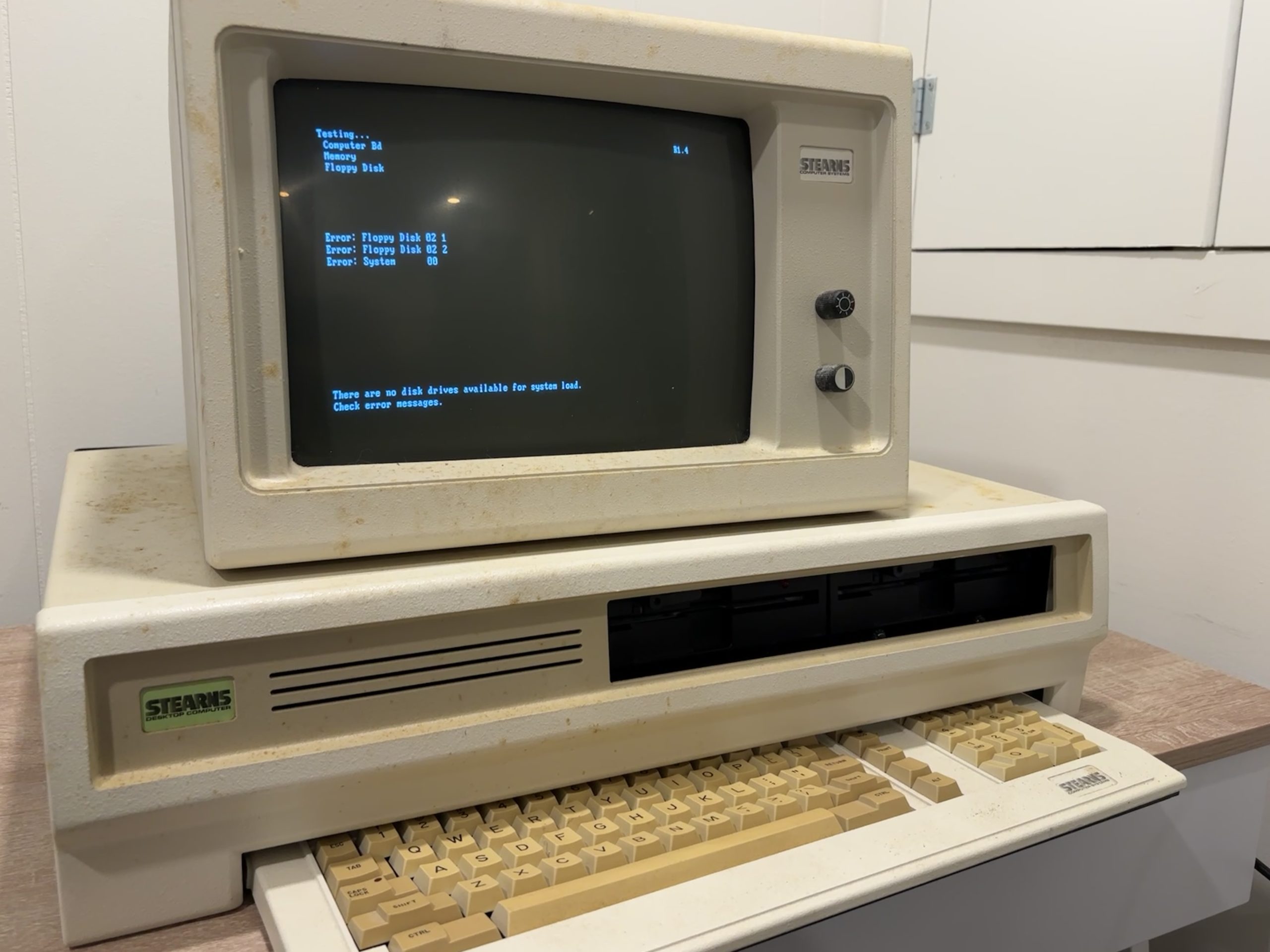 A Stearns Desktop Computer, consisting of the desktop computer base, keyboard under and in front, and monochrome white phosphor monitor on top. The monitor and computer are powered on, showing the startup screen stating that the floppy drive and system are not OK.